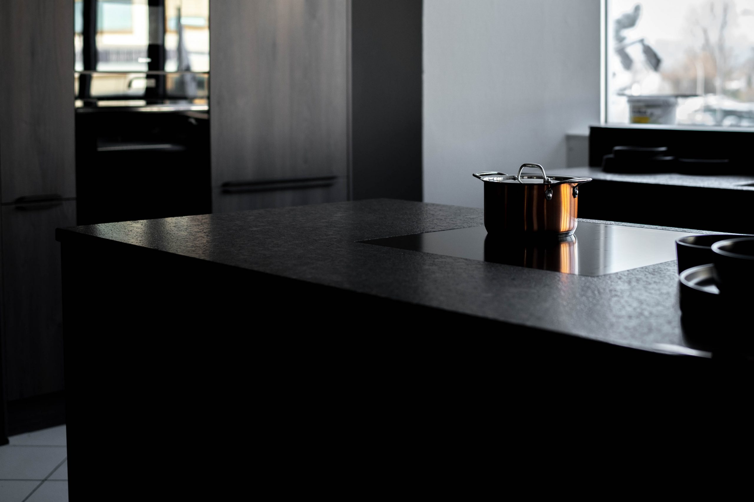 Moderne Küche mit dunklem Kücheninsel, einem Kochtopf und reflektierender Oberfläche. Minimalsitisches Design.
