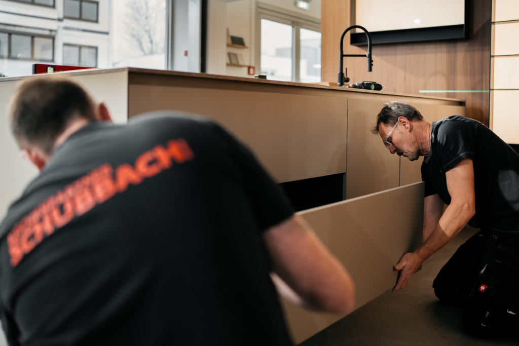 Zwei Handwerker montieren eine Küchenschublade in einem modernen Küchenraum.